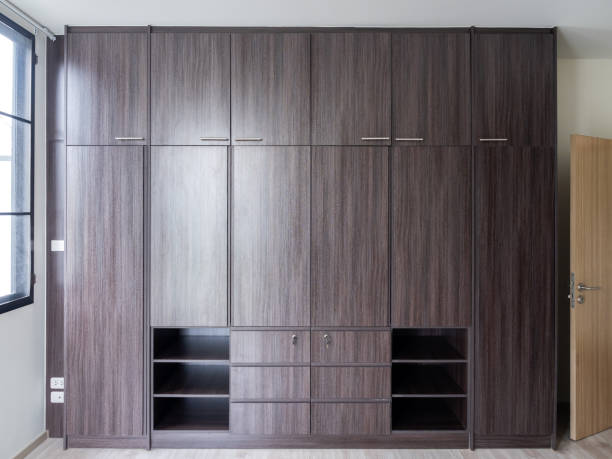 Modern huge brown wooden wardrobe in the white room, closed, front view. Built-in closet cupboard furniture on the wall near the window in the new house, simplicity home interior design.