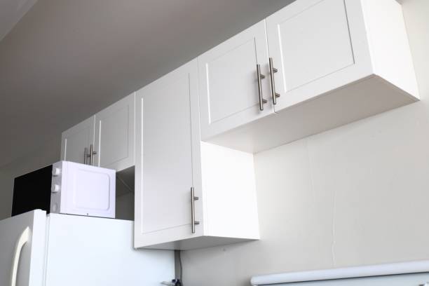 white kitchen cabinets, microwave on top of the fridge, minimalist interior, clean and simple design.